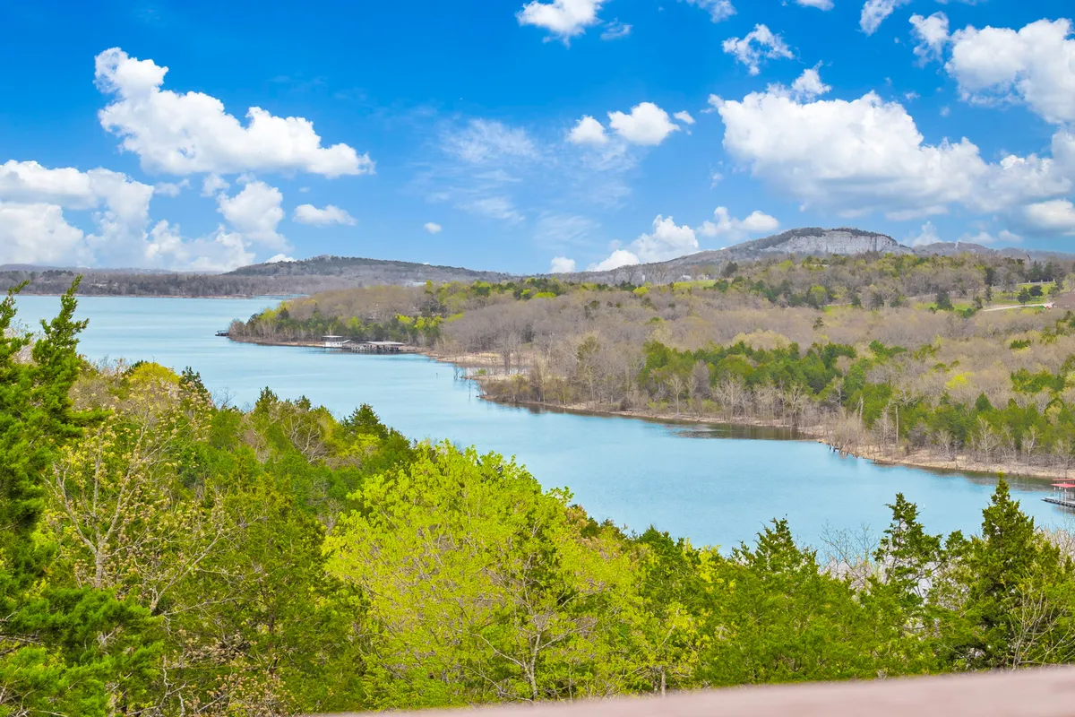 A stunning view of a tranquil blue lake with distant mountains and lush green surroundings under a sky with scattered clouds. The scene conveys a sense of peaceful seclusion, ideal for lakeside walks, quiet reflection, and inspiration from nature.