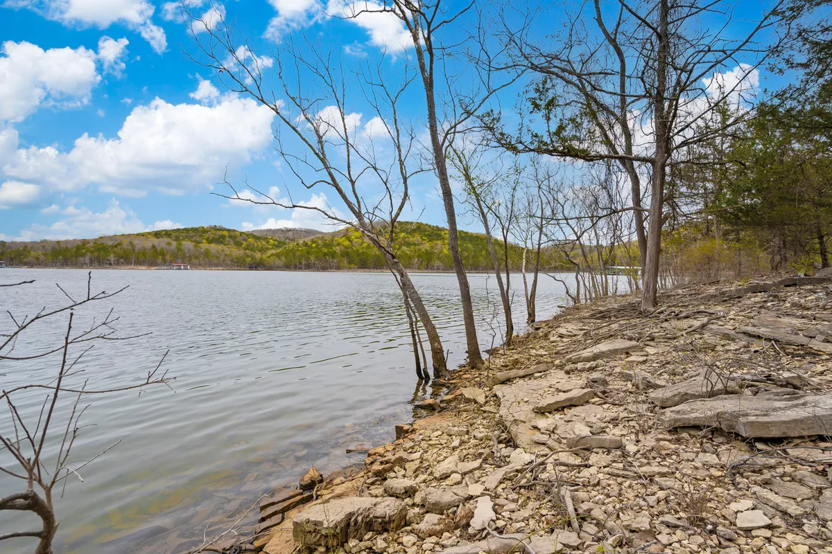 A peaceful scene featuring a calm lake bordered by a rocky shoreline and bare trees, with distant hills beyond. The landscape invites thoughtful exploration, birdwatching, and mindful time spent immersed in nature.