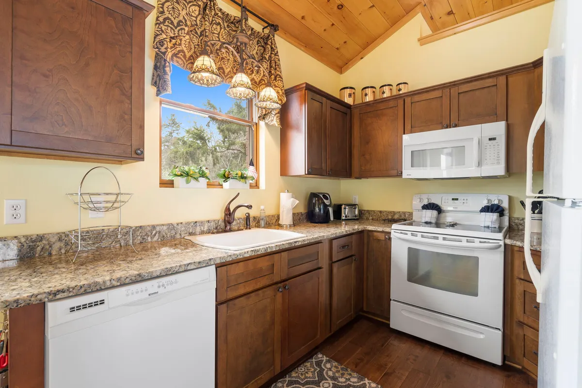 A glimpse of the fully equipped kitchen, complete with granite countertops, warm wood cabinetry, and decorative lighting. The space feels welcoming and functional, ideal for preparing casual breakfasts or elegant dinners. Subtle details like potted plants and cozy lighting add to the inviting atmosphere.